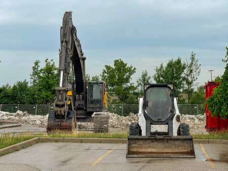 Parked excavator and skid steer on rainy day